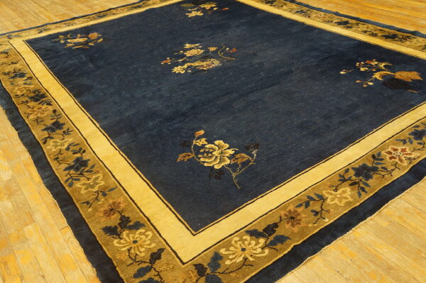 Navy blue rug with scattered gold florals and a wide yellow and olive patterned border on hardwood flooring.