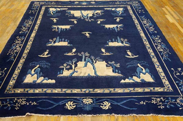 Large navy blue rug with light-colored, detailed scenic patterns of islands and boats on wood flooring.
