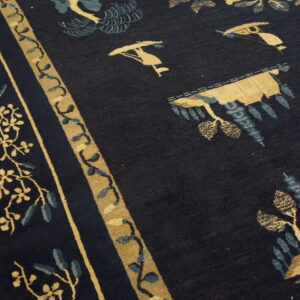 Detailed view of a plush dark blue rug with tan and blue traditional motifs next to wood flooring.