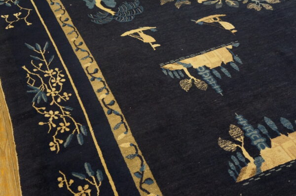 Detailed view of a plush dark blue rug with tan and blue traditional motifs next to wood flooring.