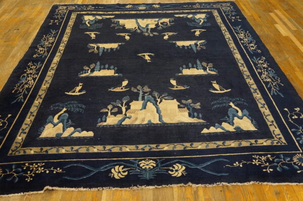 Navy blue pictorial rug with tan and light blue landscape designs sits on bright wood flooring.