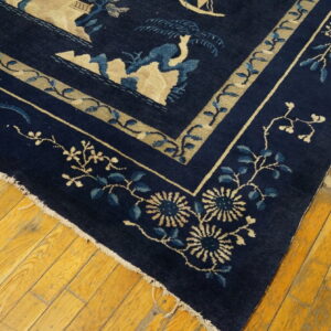 Dark blue rug with beige and light blue floral borders shown on worn, yellow plank flooring.