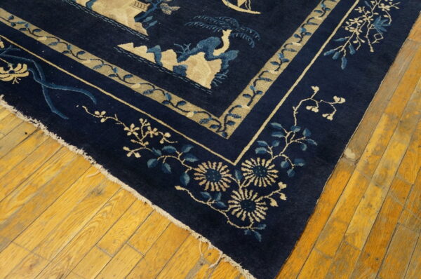 Dark blue rug with beige and light blue floral borders shown on worn, yellow plank flooring.