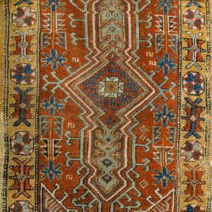 Rectangular low-pile rug with a rust, blue, and ochre geometric pattern and detailed borders.