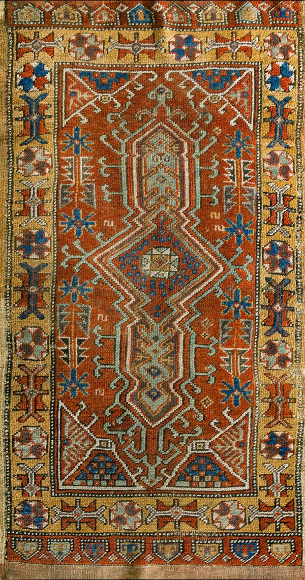 Rectangular low-pile rug with a rust, blue, and ochre geometric pattern and detailed borders.