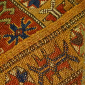 Detail of a folded rug with geometric designs in gold, rust, and blue on rustic wood.