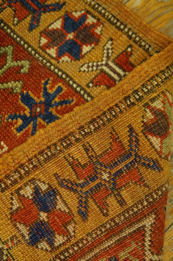 Detail of a folded rug with geometric designs in gold, rust, and blue on rustic wood.