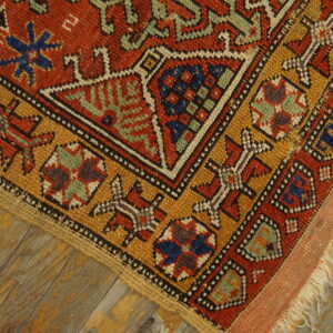 Geometric red, gold, and blue tribal patterned rug lying on distressed, painted wooden planks.