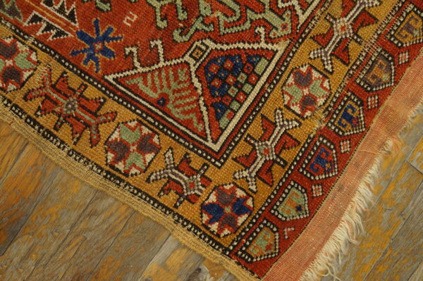 Geometric red, gold, and blue tribal patterned rug lying on distressed, painted wooden planks.