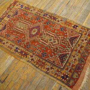 A small geometric rug in shades of rust, gold, blue, and green sits on distressed wood flooring.