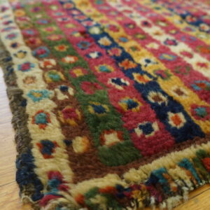 Shaggy rug detail with vibrant stripes of pink, blue, yellow, and green on light brown hardwood planks.