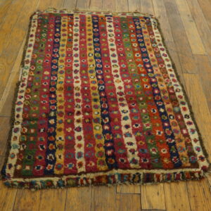High-pile multicolored rug featuring vertical striped patterns on worn light brown hardwood floors.