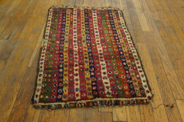High-pile multicolored rug featuring vertical striped patterns on worn light brown hardwood floors.