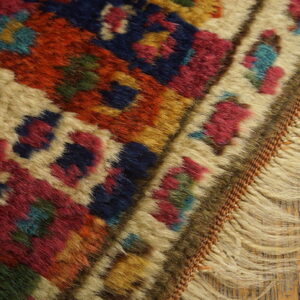 High-pile rug detail showing geometric motifs in red, navy, beige, and green, with fringe on distressed wood.