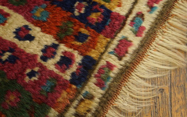 High-pile rug detail showing geometric motifs in red, navy, beige, and green, with fringe on distressed wood.