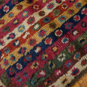 High-pile rug with colorful patterned bands in blue, magenta, gold, and green on wood floors.
