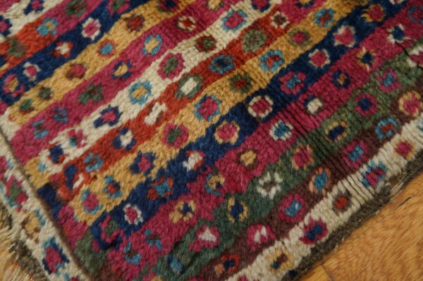 High-pile rug with colorful patterned bands in blue, magenta, gold, and green on wood floors.