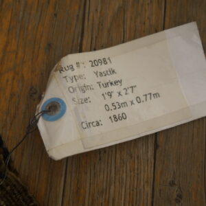 Textured, multicolored rug fibers are visible next to a descriptive white tag on rustic wood planks.