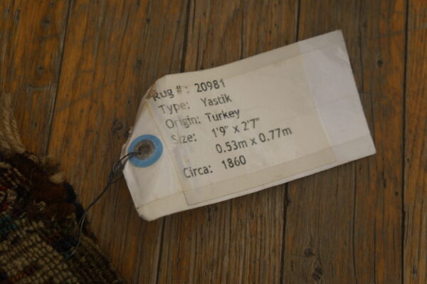 Textured, multicolored rug fibers are visible next to a descriptive white tag on rustic wood planks.