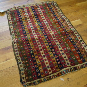 Colorful high-pile rug featuring vertical stripes of floral medallions is displayed on hardwood flooring.