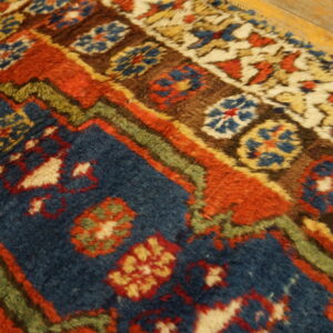 Thick pile rug in rust, indigo, and brown tribal patterns rests next to light wood floorboards.