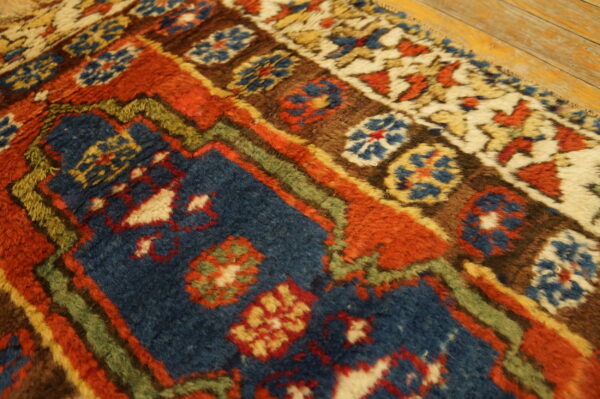 Thick pile rug in rust, indigo, and brown tribal patterns rests next to light wood floorboards.