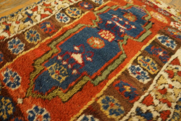 Close-up of a high-pile rug featuring blue, rust, brown, and green geometric motifs on wooden floorboards.