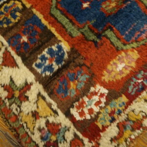 Shaggy high-pile rug corner showing rust, blue, yellow, and cream geometric patterns over warm wood floors.
