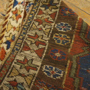 A folded rug displays low geometric pile over shaggy abstract texture on weathered wood flooring.