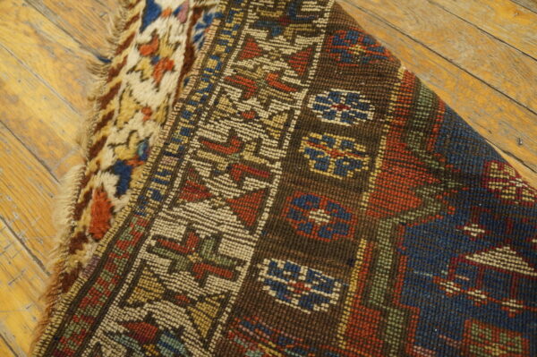 A folded rug displays low geometric pile over shaggy abstract texture on weathered wood flooring.