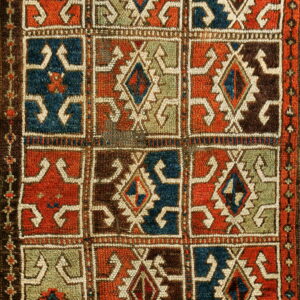 Coarse, textured rug with a repeating grid of orange, blue, green, and brown geometric designs.