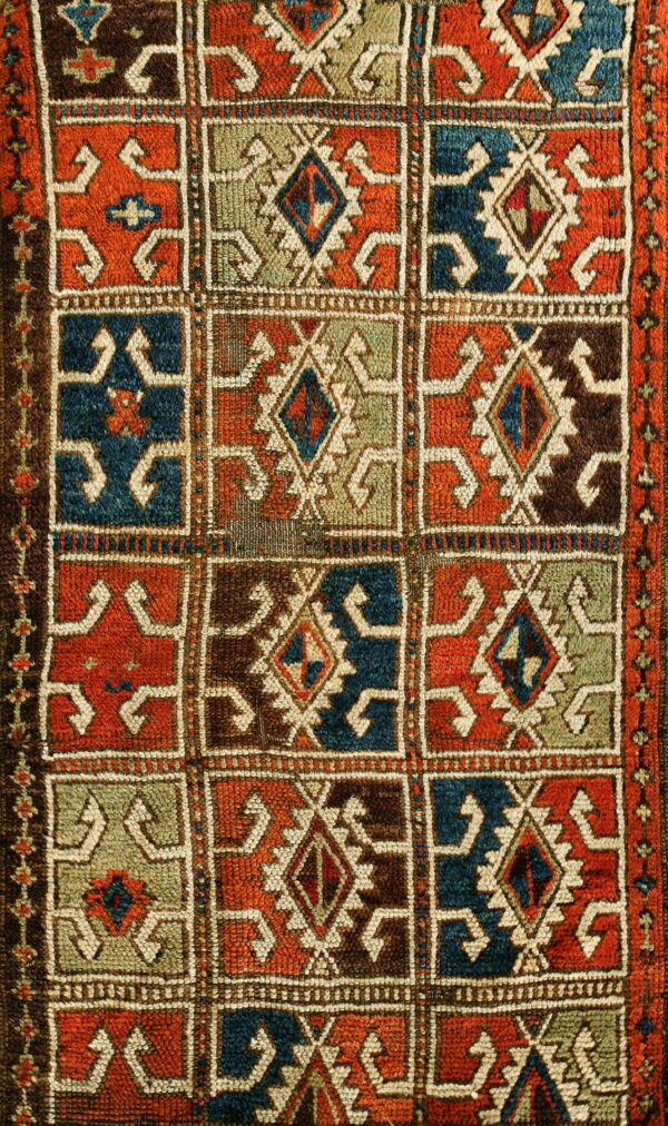 Coarse, textured rug with a repeating grid of orange, blue, green, and brown geometric designs.