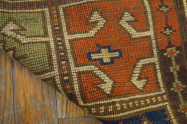 A folded geometric rug in rust, green, and cream colors rests on distressed light wood flooring.