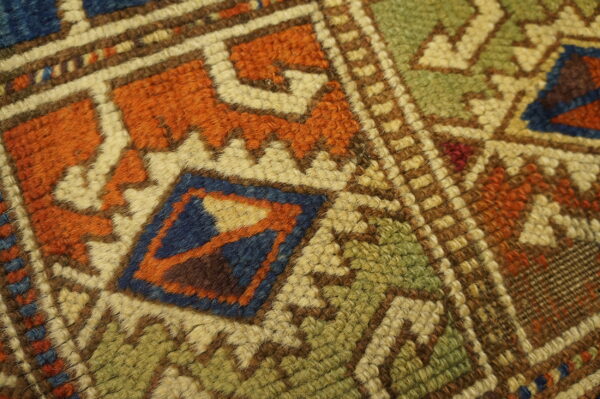 High-texture rug detail showing chunky knots forming tribal geometric patterns in orange, green, blue, and brown.