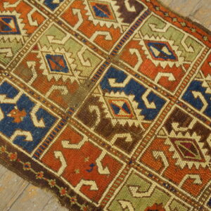 Low-pile rug with geometric repeating diamonds in rust, blue, green, and brown, laid on distressed wood.
