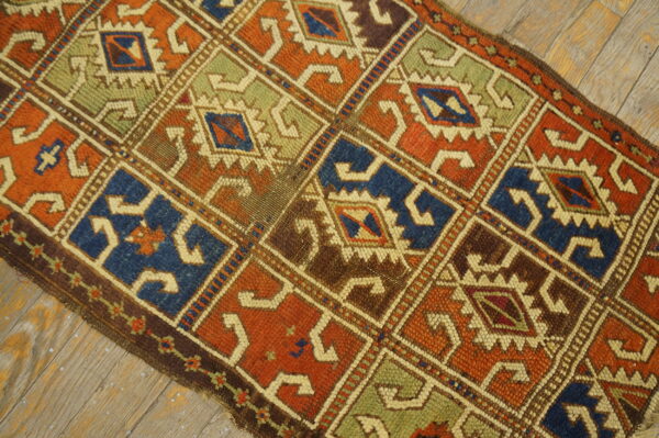 Low-pile rug with geometric repeating diamonds in rust, blue, green, and brown, laid on distressed wood.