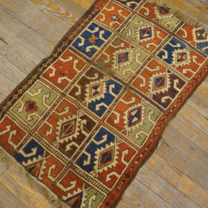 Geometric grid pattern rug in deep blues, oranges, greens, and browns rests on distressed wood flooring.