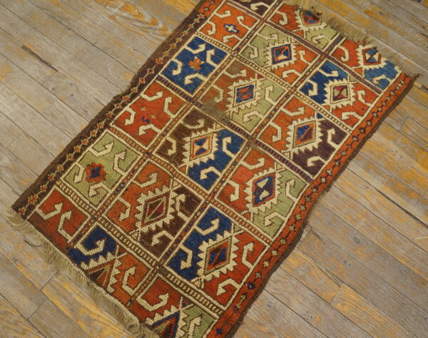 Geometric grid pattern rug in deep blues, oranges, greens, and browns rests on distressed wood flooring.