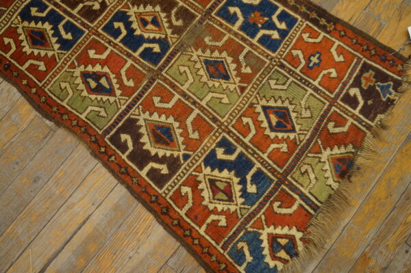 Rust, blue, and green geometric rug runner with diamond motifs lies on worn wood planks.