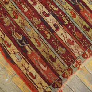 Low-pile rug with geometric stripes in rich red, beige, and olive on distressed hardwood floors.