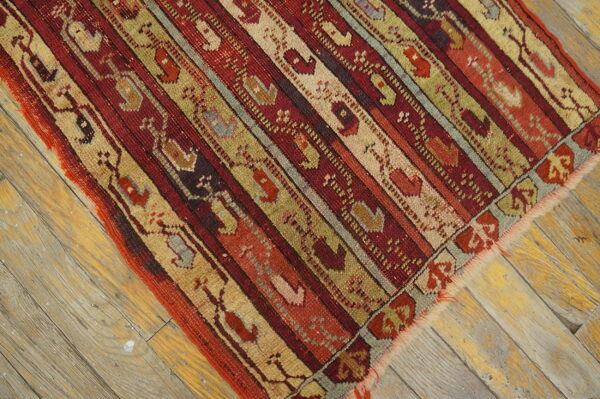 Low-pile rug with geometric stripes in rich red, beige, and olive on distressed hardwood floors.