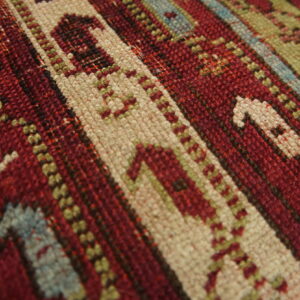 Tight weave rug showing geometric stripes and motifs in red, cream, olive, and light blue colors.
