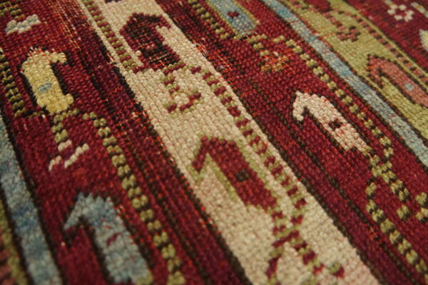 Tight weave rug showing geometric stripes and motifs in red, cream, olive, and light blue colors.