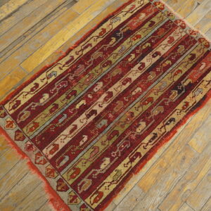 Red, gold, and green striped rug with complex geometric patterns displayed on worn wood flooring.
