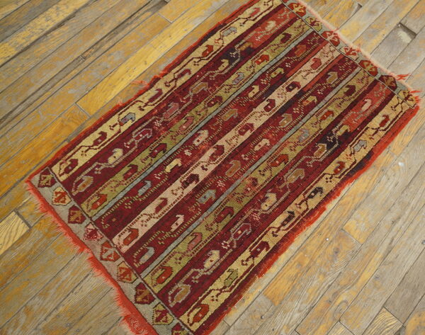 Red, gold, and green striped rug with complex geometric patterns displayed on worn wood flooring.