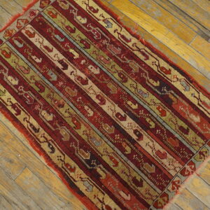 Red, olive, and beige striped geometric rug rests on worn yellow wooden floorboards.