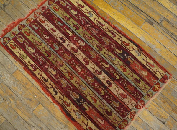 Red, olive, and beige striped geometric rug rests on worn yellow wooden floorboards.