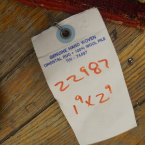 Close-up of a high-pile red, tan, and maroon patterned rug edge on rustic wood plank flooring.
