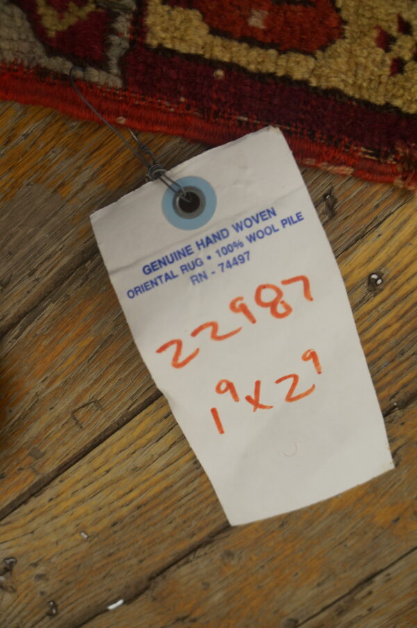Close-up of a high-pile red, tan, and maroon patterned rug edge on rustic wood plank flooring.