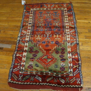 High pile rug featuring rust, olive green, blue, and cream geometric tribal motifs on wood floor.